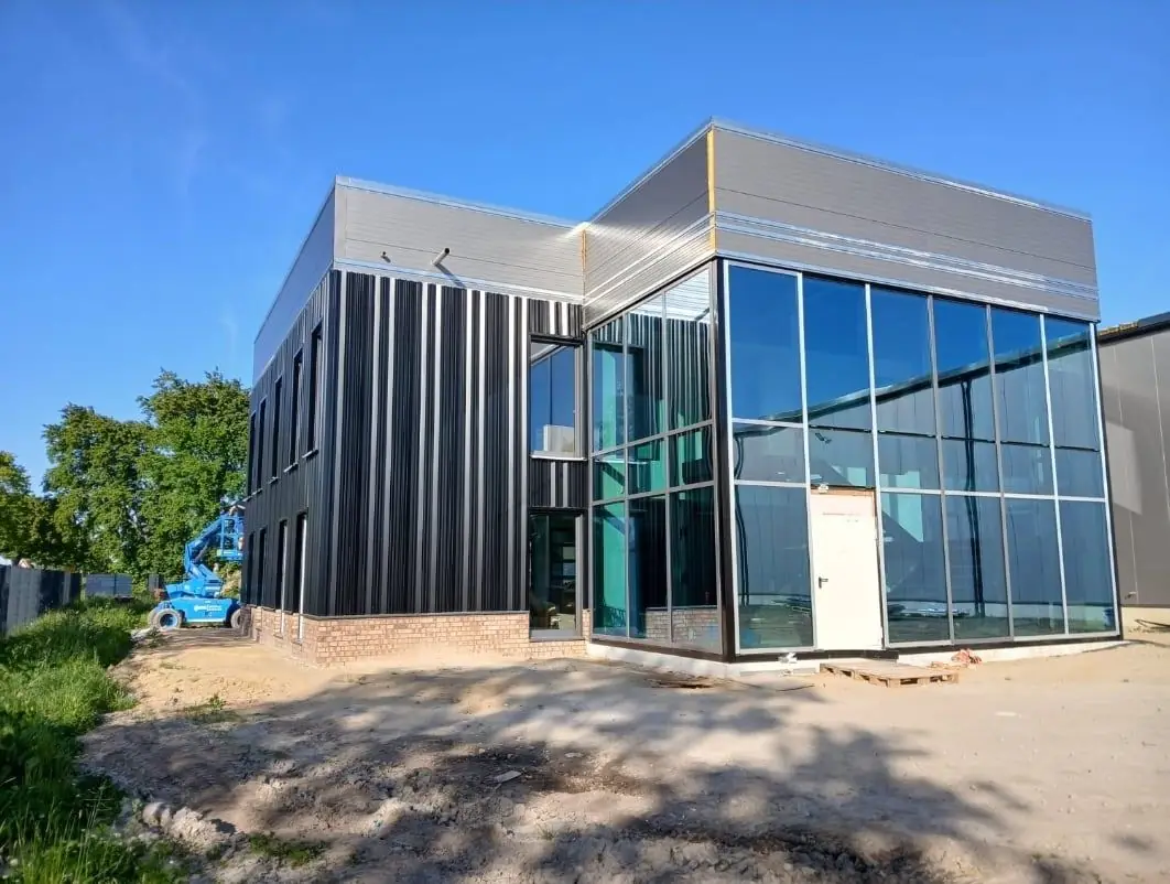 Fertiggestelltes Gewerbegebäude mit dunkler Metallfassade und Glasvorbau auf der Baustelle